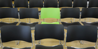 Ein grüner Stuhl inmitten von schwarzen Stühlen